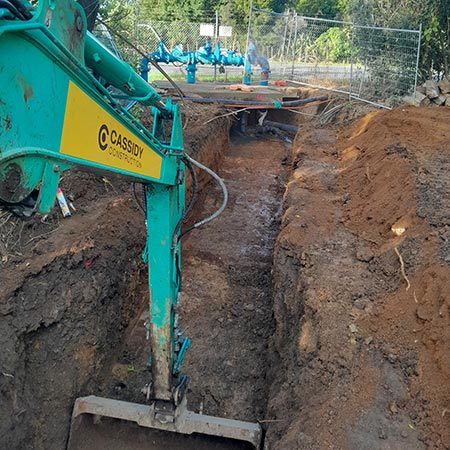 close up of cassidy excavator arm digging trench for potable water pipework